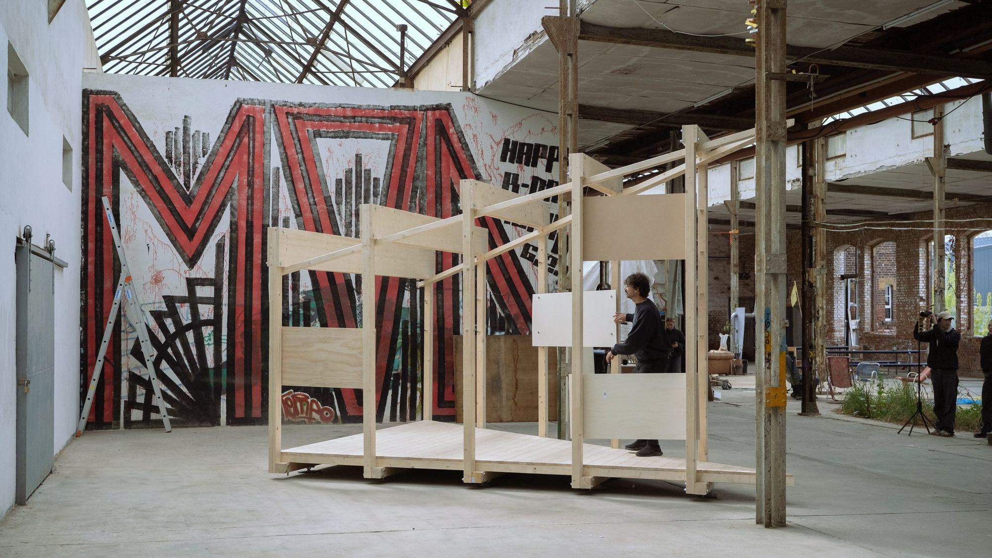 Holzpavillon mit Paneelen vor dem großen Wandbild in der Halle